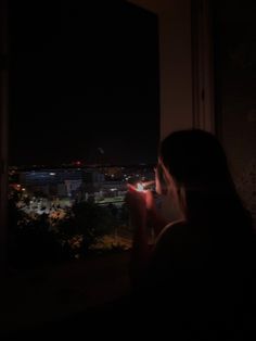 a woman is looking out the window at night with her cell phone to her ear