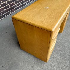 a wooden bench sitting on top of a sidewalk next to a brick wall and cement floor