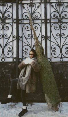 a woman sitting on a bench next to a tree in front of a building with wrought iron doors