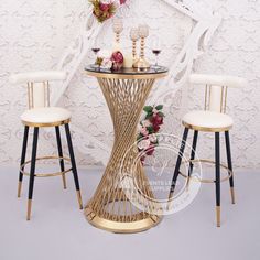 two stools and a table with flowers on it in front of a white wall