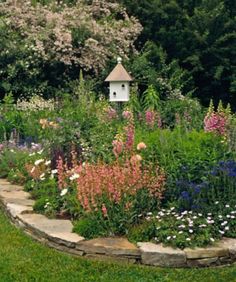 a garden filled with lots of flowers next to a birdhouse on top of a hill