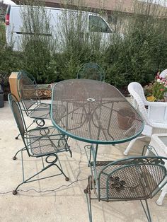 an outdoor table and chairs are set up on the concrete ground in front of some bushes