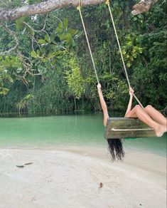 a woman hanging from a tree swing over the water in a jungle area with green trees