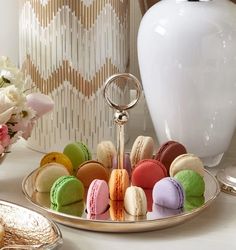 a tray with macaroons on it next to a white vase and some flowers