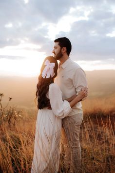 a man and woman kissing in the middle of an open field with tall grass at sunset