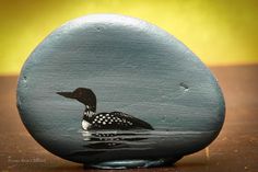 a painted rock with a duck in the water on it's side, sitting on a table