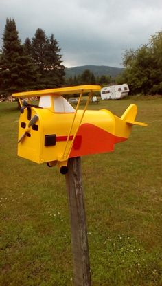 a yellow airplane shaped mailbox sitting on top of a wooden post in a field