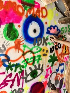 a woman standing in front of a wall covered in colorful spray paint and graffiti writing on it