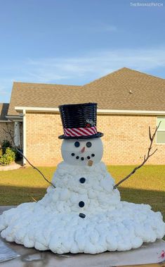 a snowman made out of cotton balls in front of a house with a top hat on