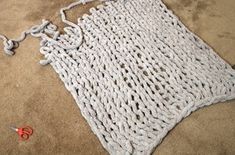 a white crocheted piece of cloth on the ground with scissors and thread next to it