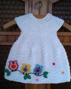 a white dress with flowers on it is hanging from a wooden hanger in front of a brick wall