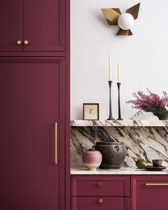 a kitchen with purple cabinets and marble counter tops, gold accents on the wall above