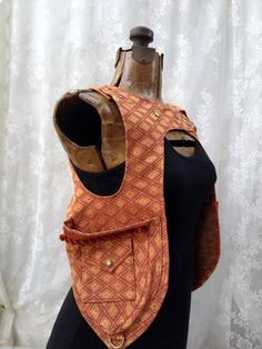 a mannequin with an orange and brown vest on it's back, next to a white curtain