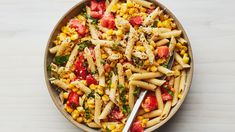 a bowl filled with pasta and vegetables on top of a wooden table next to a fork