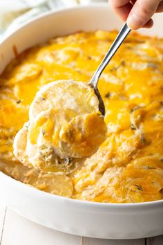 a spoonful of cheesy potato casserole being lifted from a white dish