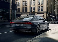 the rear end of a black car driving down a street in front of tall buildings