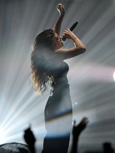 a woman holding a microphone up to her mouth while performing on stage with other people in the background