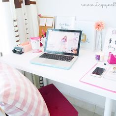 a laptop computer sitting on top of a white desk next to a pink pillow and chair