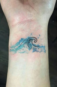 a small wave tattoo on the wrist, with blue water splashing down it's side