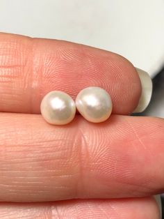 two white pearls sitting on top of a persons finger in front of a cup and saucer