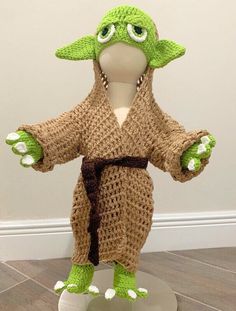 a crocheted yoda doll is posed on top of a white base and holds his arms out