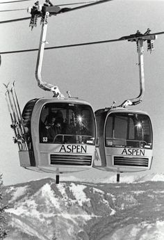 two ski lift cars with skiers on them going down the mountain side in black and white