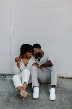 a man and woman sitting on the ground next to each other with their arms around each other