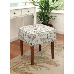 a white and brown footstool sitting on top of a rug next to a potted plant