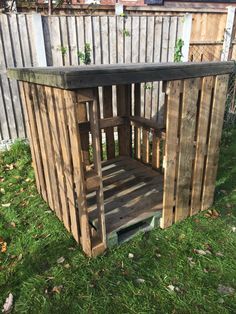 a wooden bench made out of pallets in the grass next to a fence and building