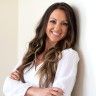 a woman with long hair standing in front of a white wall and smiling at the camera