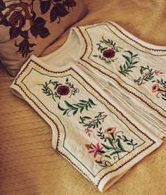 two white blouses sitting on top of a bed next to pillows and a pillow