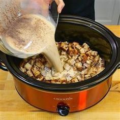 a person pouring something into a crock pot filled with food on top of a wooden table