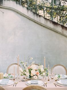 the table is set with white and pink flowers, candles, and place settings for dinner