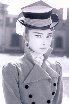 a black and white photo of a woman in a trench coat with a hat on her head