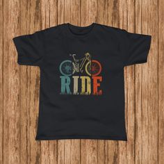 a black t - shirt with the words ride on it and a bicycle in rainbow colors