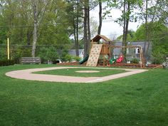 a baseball field with a slide and play area in the back ground, surrounded by trees