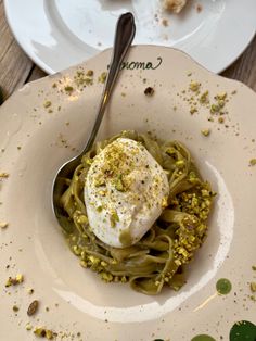 a white plate topped with pasta covered in pesto sauce and an egg on top