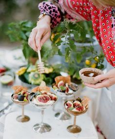 a woman is holding a spoon over some desserts on a white table with flowers in the background