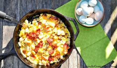 an iron skillet with eggs and bacon in it next to a bowl on a wooden table