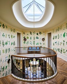 a circular room with wallpapered walls and wooden flooring has a skylight above the spiral staircase