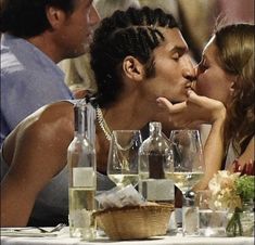 a man and woman kissing each other at a table with wine glasses on the table