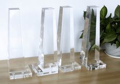 three clear vases sitting on top of a wooden table next to a potted plant