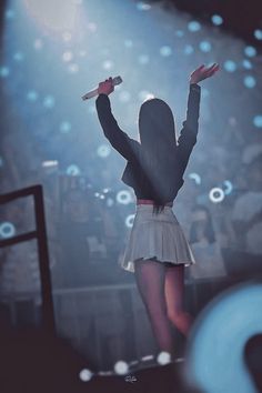 a woman in a short skirt is on stage with her arms up and hands raised above her head