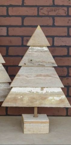 two wooden christmas trees sitting next to each other in front of a brick wall,