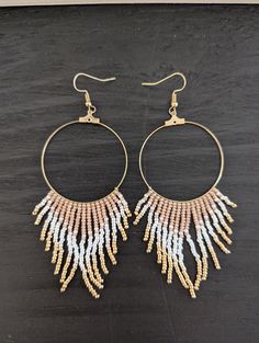 a pair of gold hoop earrings with white and pink beaded fringes on them