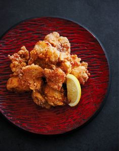 a red plate topped with fried food next to a lemon wedge