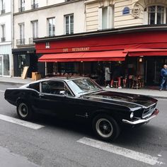 an old black car parked on the side of the road in front of a restaurant