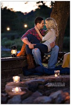 a man and woman sitting on a bench in front of a tree with lit candles