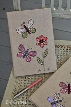 two embroidered notebooks sitting on top of a table next to a pen and pencil