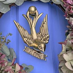 a blue door with a gold bird on it's side and flowers around it